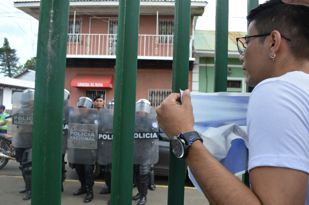 El ex reo político Luis Miguel Lesage saca la bandera de Nicaragua el 25 de agosto de 2019 ante el asedio de la Policía durante una feria a beneficio de los opositores. Él y sus dos hermanos, también ex presos del gobierno, hacen camisetas con mensajes honrando a los fallecidos durante la represión del gobierno. Crédito: Stereo romance