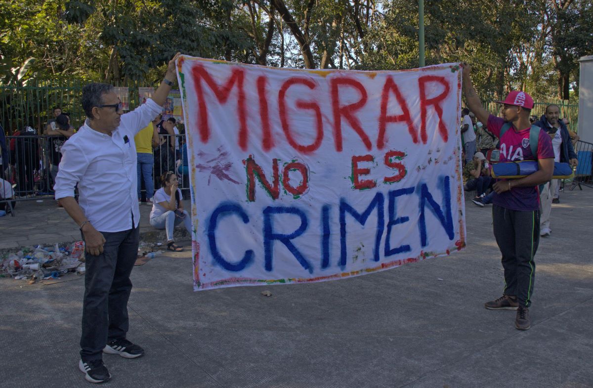 Dos migrantes sostienen un cartel que dice "Migrar no es un crimen", afuera de la Comisión Mexicana de Ayuda a Refugiados.