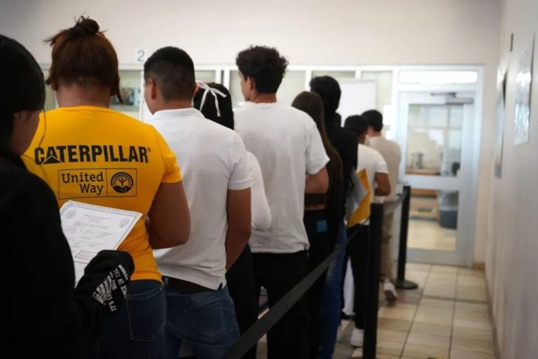 Migrantes latinoamericanos hacen fila en una oficina estadounidense.