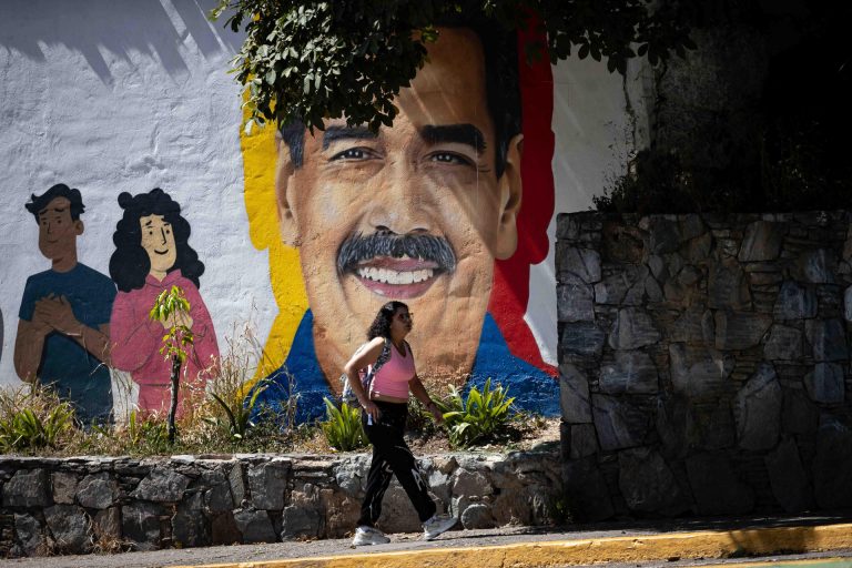 Una mujer camina frente a un mural con la imagen de Nicolás Maduro.