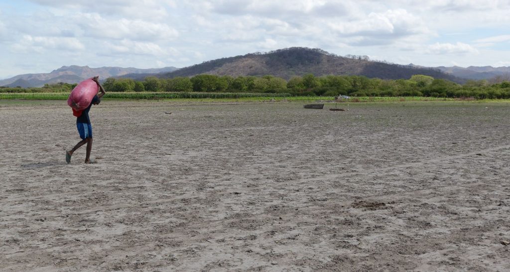 Un ciudadano camina y carga un saco por un campo seco