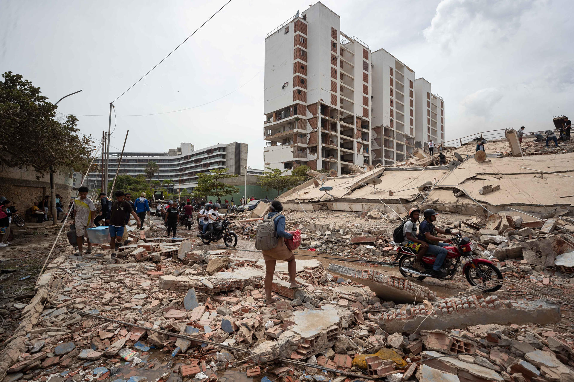 Personas caminan por escombros de edificios afectados por terremotos en La Guaira
